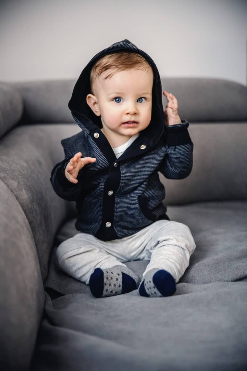Cute Little Blond Boy With Blue Eyes Sitting Sofa Living Room With Hoodie
