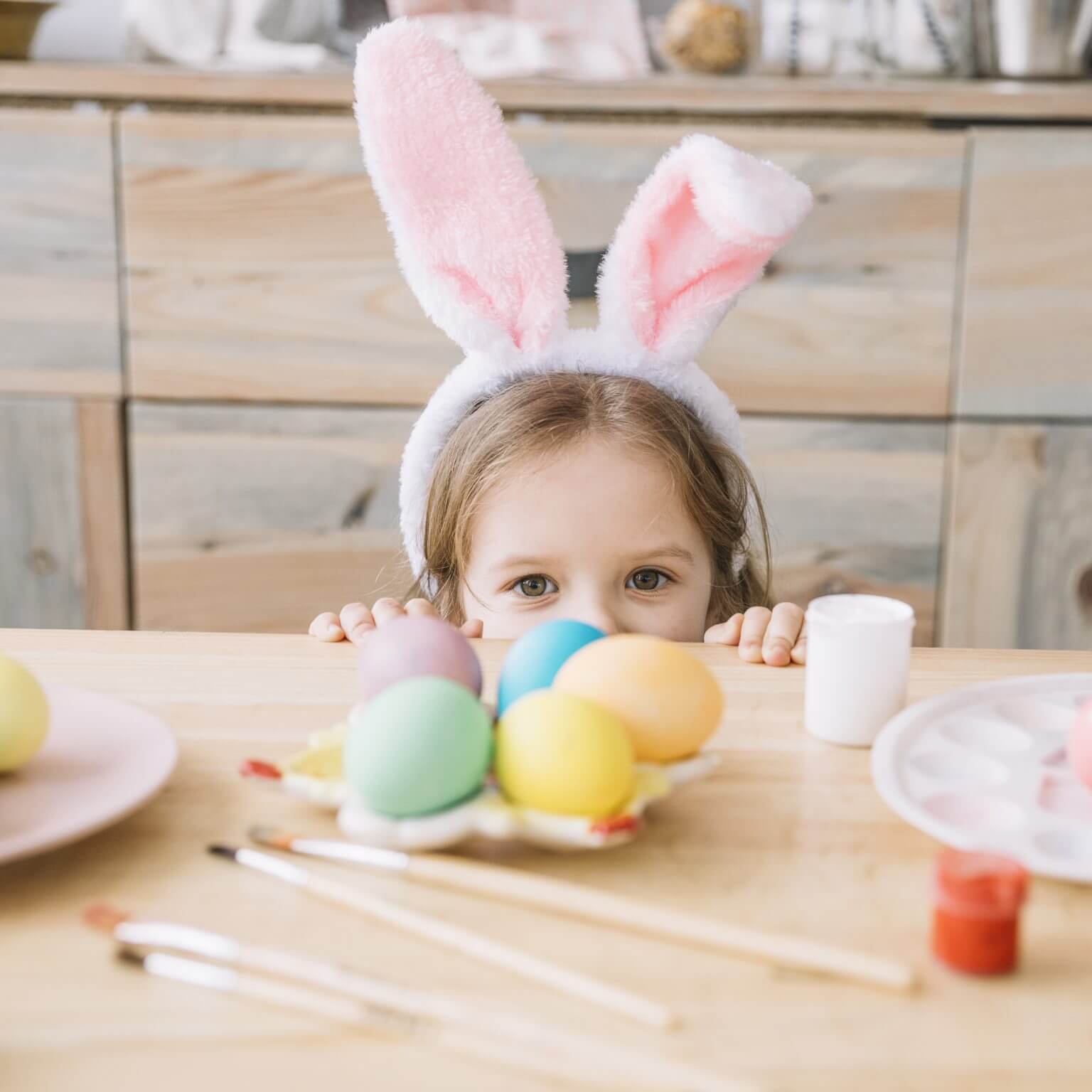 little girl wearing bunny ear headband looking at easter eggs